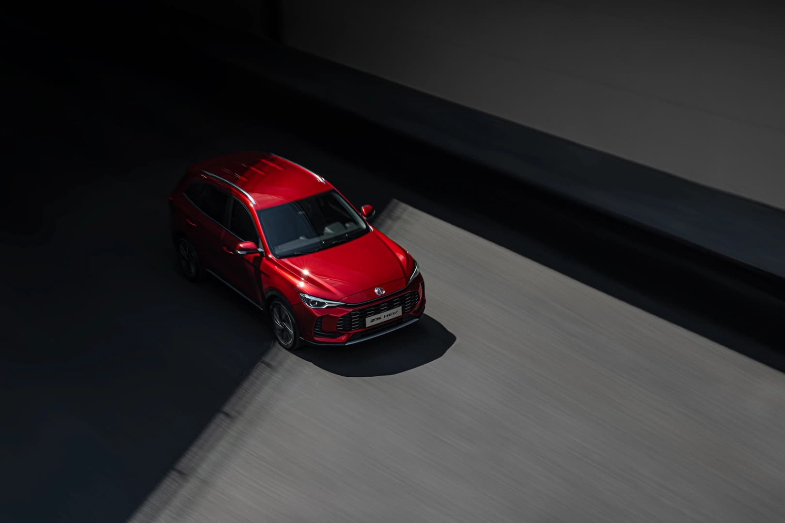 Czerwony SUV marki MG ZS HEV jadący po zacienionej drodze w świetle dziennym